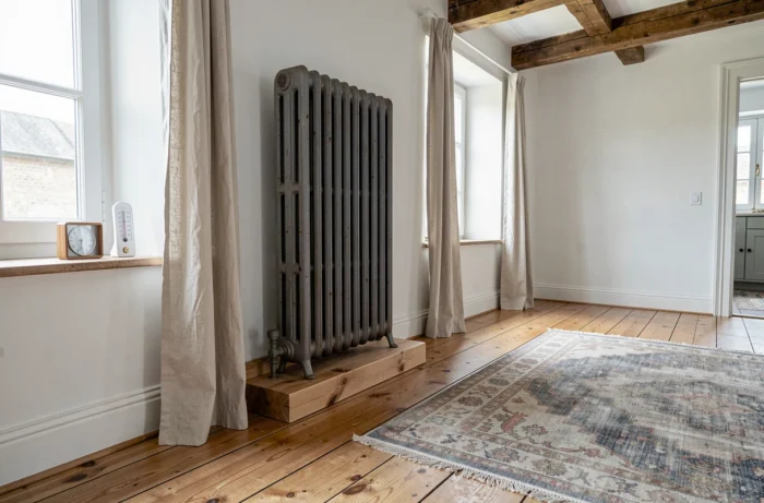 Vue d'ensemble d'un salon de maison de campagne avec un radiateur en fonte sur un socle en bois protégeant un plancher en pin ancien