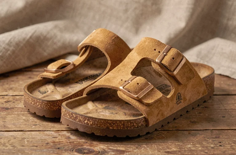 Paire de sandales Birkenstock Arizona en daim beige posée sur une surface en bois rustique, mettant en valeur le semelle en liège et les boucles iconiques